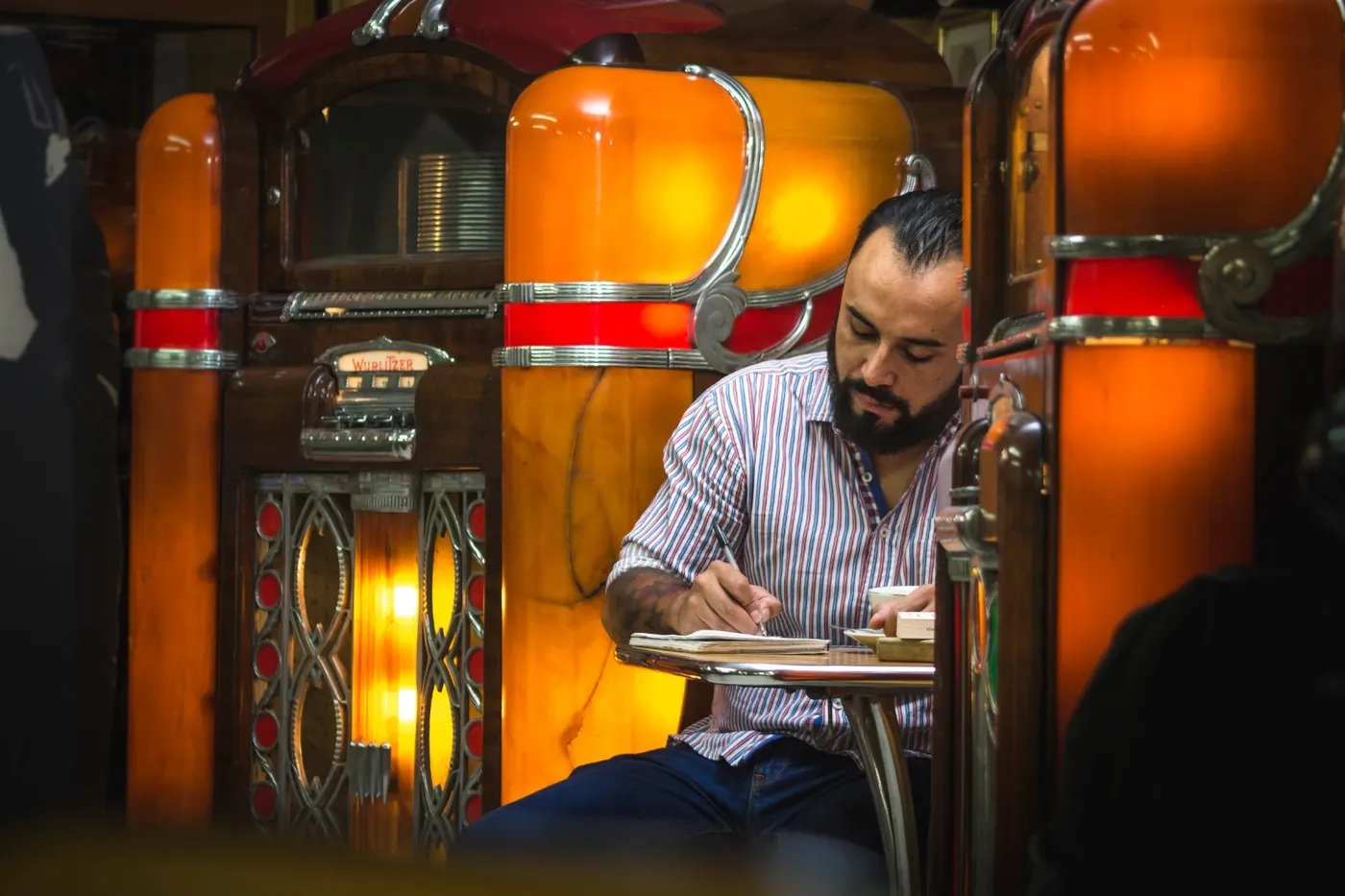 Víctor Belmonte escribiendo en un café, con rocolas antiguas de fondo